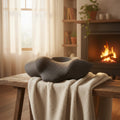 Coussin cervical chauffant RelaxCocoon gris à texture matelassée posé sur un banc en bois devant une cheminée